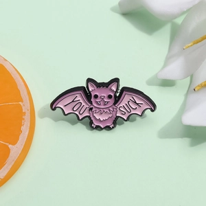 Pink and purple bat enamel pin featuring "YOU SUCK" text on a mint green background