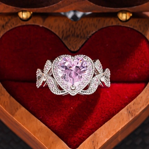 Macro shot of silver ring with pink heart gem on red velvet within a heart jewelry box
