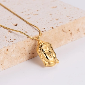 Golden Buddha head pendant necklace with snake chain on light beige stone background