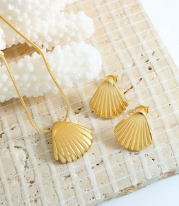 Flat lay of gold seashell necklace and earrings set on stone and coral background