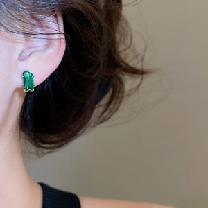 Close-up of model wearing rectangular green emerald stud earrings in silver finish