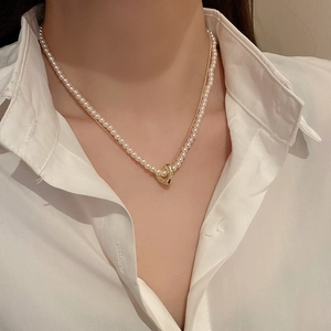 Double-layer necklace featuring white pearls and a golden heart pendant on model