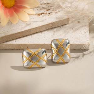 Macro shot of silver square earrings with gold diamond pattern on a travertine stone