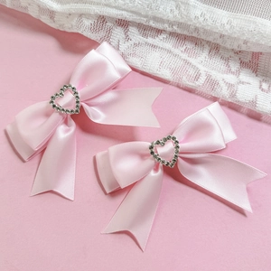 Détail de pinces à cheveux nuds en satin rose avec strass en cœur et longs rubans