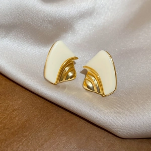 Macro view of geometric gold earrings with cream resin inlay on satin fabric