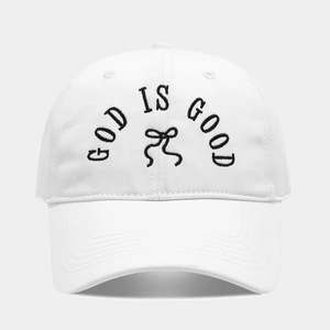 Close-up of God Is Good embroidery and black bow detail on a white cotton baseball cap