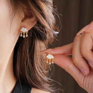 Close-up of golden cloud earrings with white mother of pearl and hanging zircon teardrops