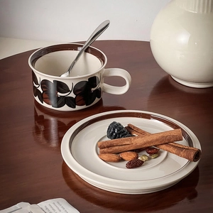 Detail of vintage hand-painted ceramic coffee cup with dark leaf patterns on wooden table