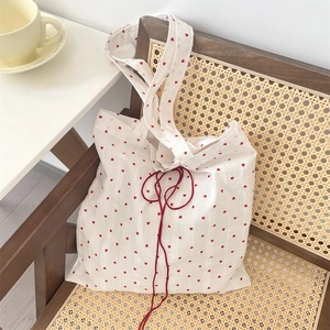 Detail of white canvas tote bag with red heart pattern and drawstring on chair