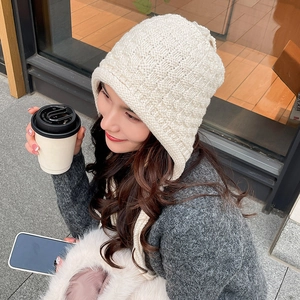 Close-up of cream knit beanie with earflaps and textured chunky knit pattern