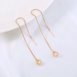 Detailed view of long gold tassel earrings with hollow sphere and zircon pendants on silk