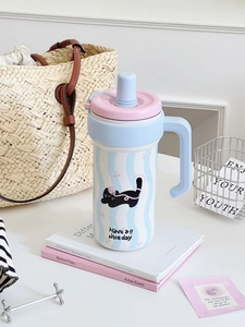 Detail of blue insulated tumbler with handle and cute cat graphic in cozy setting