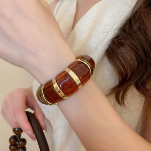 Detail of amber acrylic bracelet with golden metal accents on female wrist