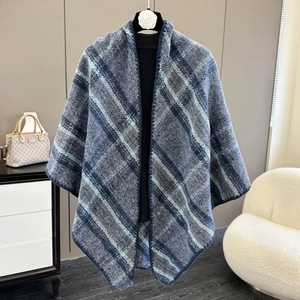 Detail of blue plaid knit shawl poncho draped on a model stand in a bright room
