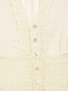 Close-up of cream lace shirt featuring V-neckline with pearl buttons and textured fabric