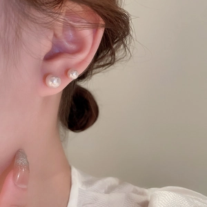 Detailed close-up of elegant white pearl stud earrings on ear showing two sizes