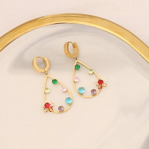 Macro shot of gold-plated teardrop earrings with colorful crystals on marble tray