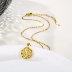Close-up of golden round pendant with letter I, beaded edge and matte finish