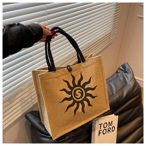 Close-up of linen tote bag featuring a sun pattern and black woven rope handles