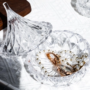 Elegant glass jewelry storage jar with faceted lid containing pearl necklace and watch