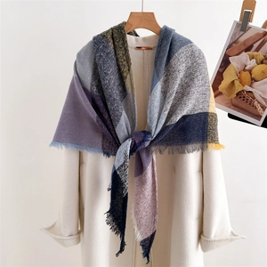 Fashionable colorful plaid tassel scarf draped over a white coat on a wooden hanger