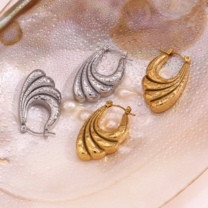 Macro view of gold and silver wave-shaped hoop earrings on a wet shell background