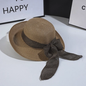 Detail of light brown straw hat with a thick dark brown ribbon bow on a white surface