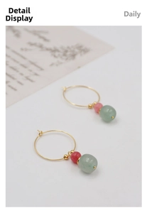 Detail of gold hoop earrings with green and red jade-like beads on a minimalist background