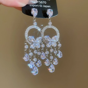 Détail de boucles d'oreilles argentées à pampilles avec motifs papillon et zircons gouttes
