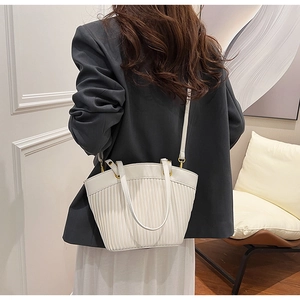 Detail shot of white pleated bucket bag with dual handles and slender shoulder strap