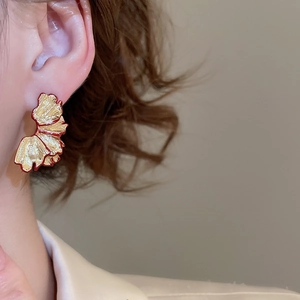 Close-up of golden petal earrings with red trim details on a model's ear