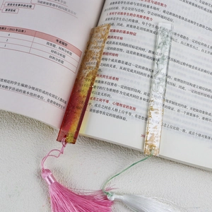 Detail of DIY resin bookmarks with gold foil, dried flowers, and colorful tassels on a book