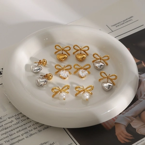 Set of stainless steel bow and heart earrings with zircon and pearls on a white plate