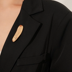 Close-up of a long golden organic streamline metal brooch on a black blazer jacket