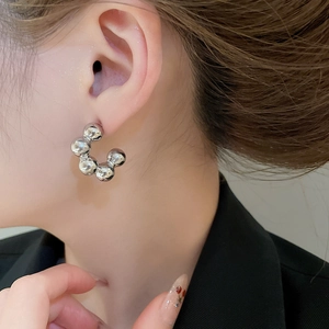 Detail of silver C-shape bubble bead earrings on model showing minimalist metal texture