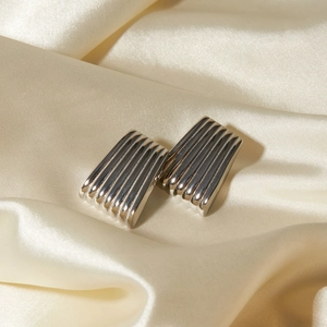 Close-up of silver stainless steel earrings with vertical stripe texture on silk fabric