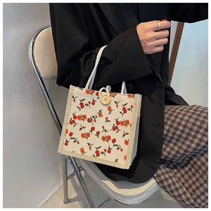 Close-up of cream canvas handbag with red floral print and wooden button closure