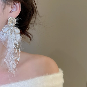 Close-up of elegant crystal bow earrings with feather tassels worn by a model