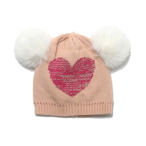 Detail of pink knitted kids hat with white faux fur pom poms and glitter heart patch