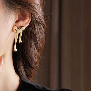 Close-up of a model wearing high-polish golden lava heart earrings on a dark background