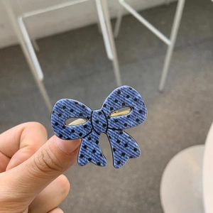 Detailed close-up of blue polka dot bow hair clip with gold metal duckbill attachment