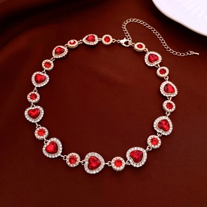 Détail d'un collier doré avec pierres rouges en cœur et strass sur tissu velours