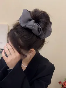 Detail showing oversized dark gray satin bow hair scrunchie worn on a bun hairstyle