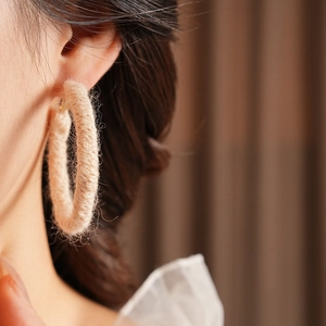 Dettaglio di un grande orecchino a cerchio in rafia beige intrecciata indossato da modella