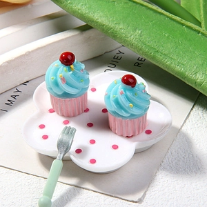 Miniature resin blue cupcakes with cherry topping on a white plate with a green fork
