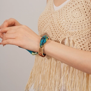 Close-up of a teal silk scarf bracelet with gold metal fastener on model's wrist