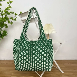 Detail shot of green and white wavy stripe knit tote bag on a white chair