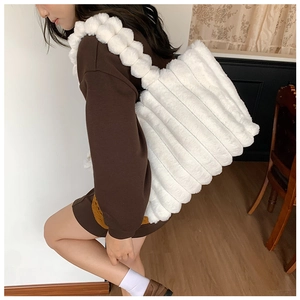 Detail of white plush striped shoulder bag with fluffy ball strap shown on a model