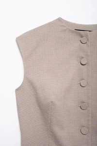 Close-up of beige brown plaid vest featuring fabric-covered buttons and textured material