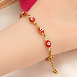 Detalle de pulsera dorada con dijes rojos del ojo del mal en una muñeca real